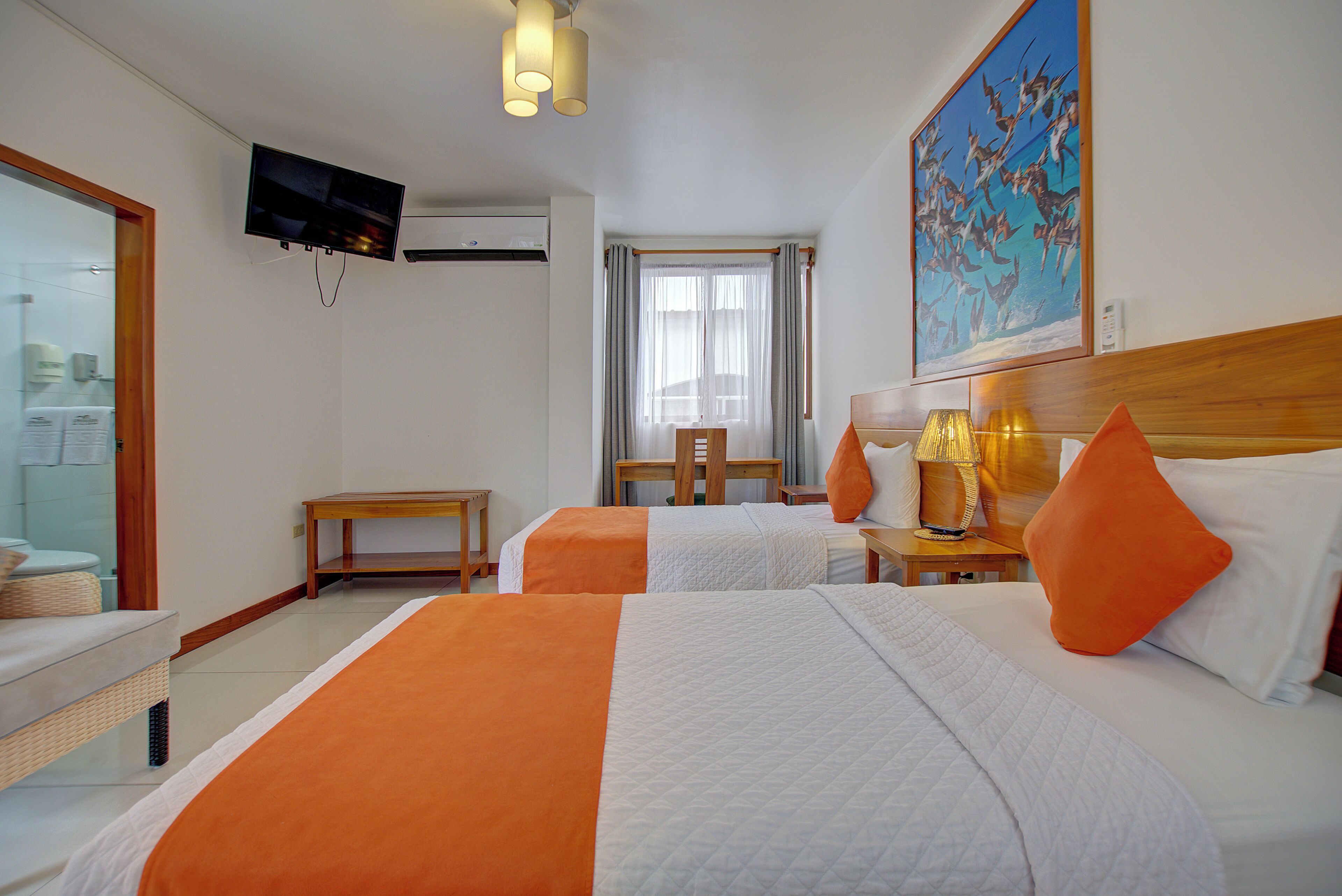 Ein Hotelzimmer mit zwei Betten, einem Fernseher, einem Gemälde und einem Fenster mit Vorhängen.