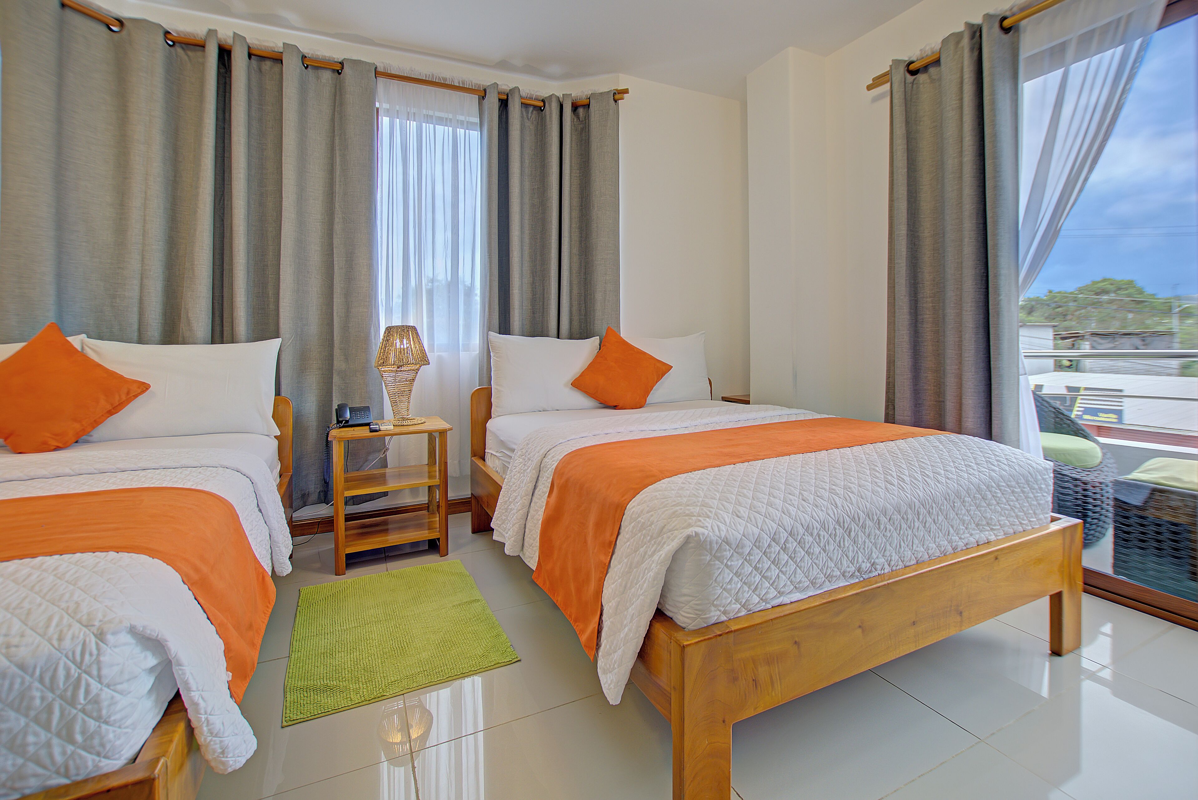 A hotel room with two beds, a small table, and a view of the outside.