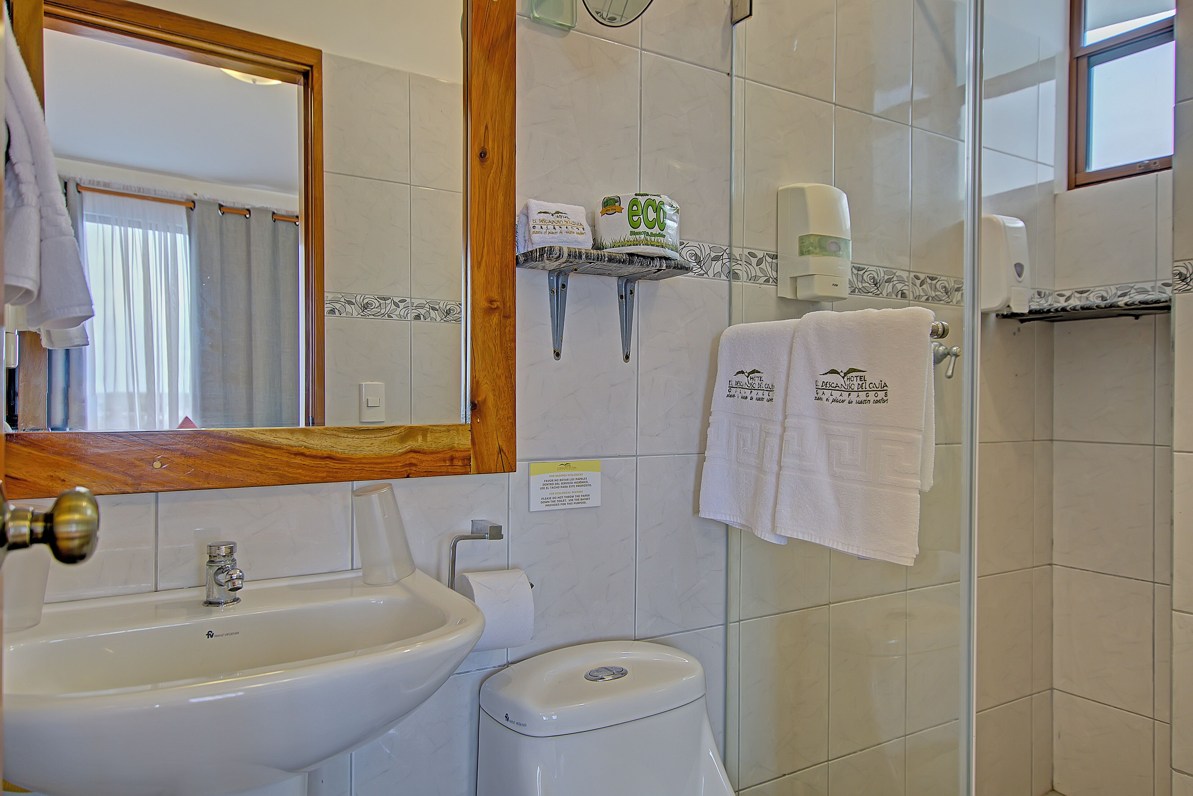 A bathroom with a sink, toilet, and mirror. There are towels hanging on the wall and a soap dispenser.