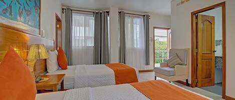 Habitación de hotel con dos camas, una zona de estar y un ventanal con cortinas.