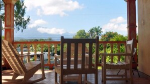 A covered outdoor area with tiled flooring, wooden chairs, and a view of the sky and greenery. - Hotel Molina (La Ceiba)