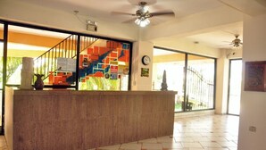 A reception area with a curved reception desk, a staircase with colorful railings, and large windows offering a view of the outdoors. - Hotel Molina (La Ceiba)