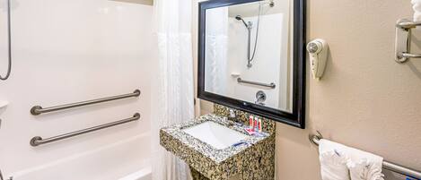 A bathroom with a white bathtub, a granite sink, a mirror, and a towel rack.