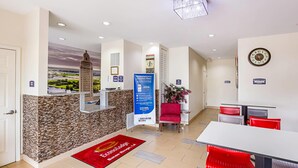 A hotel lobby with a reception desk, a clock, a red chair, and a dining area with red and grey chairs. - Econo Lodge Baton Rouge University Area (Baton Rouge)