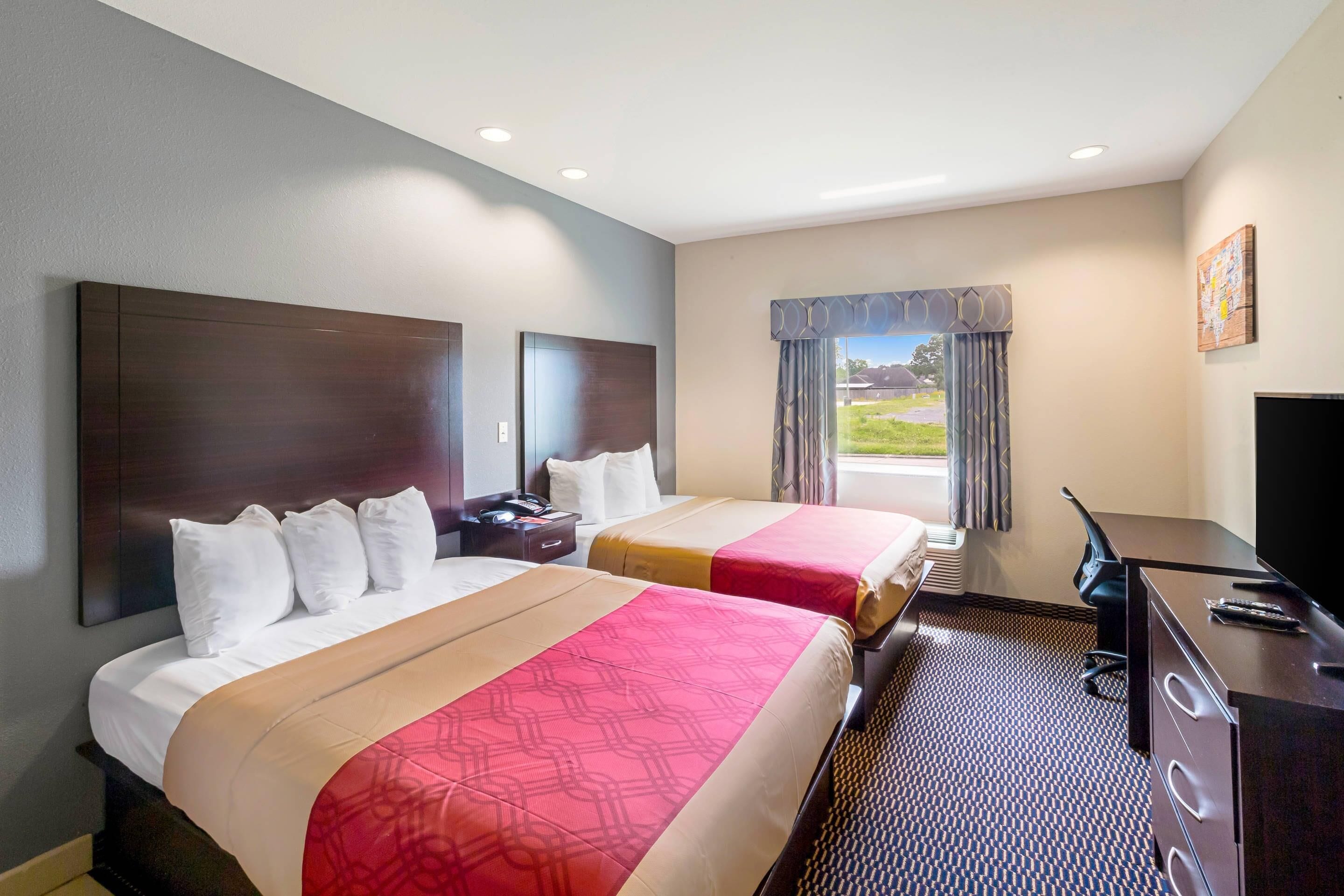 A hotel room with two beds, a desk, a television, and a window with curtains.
