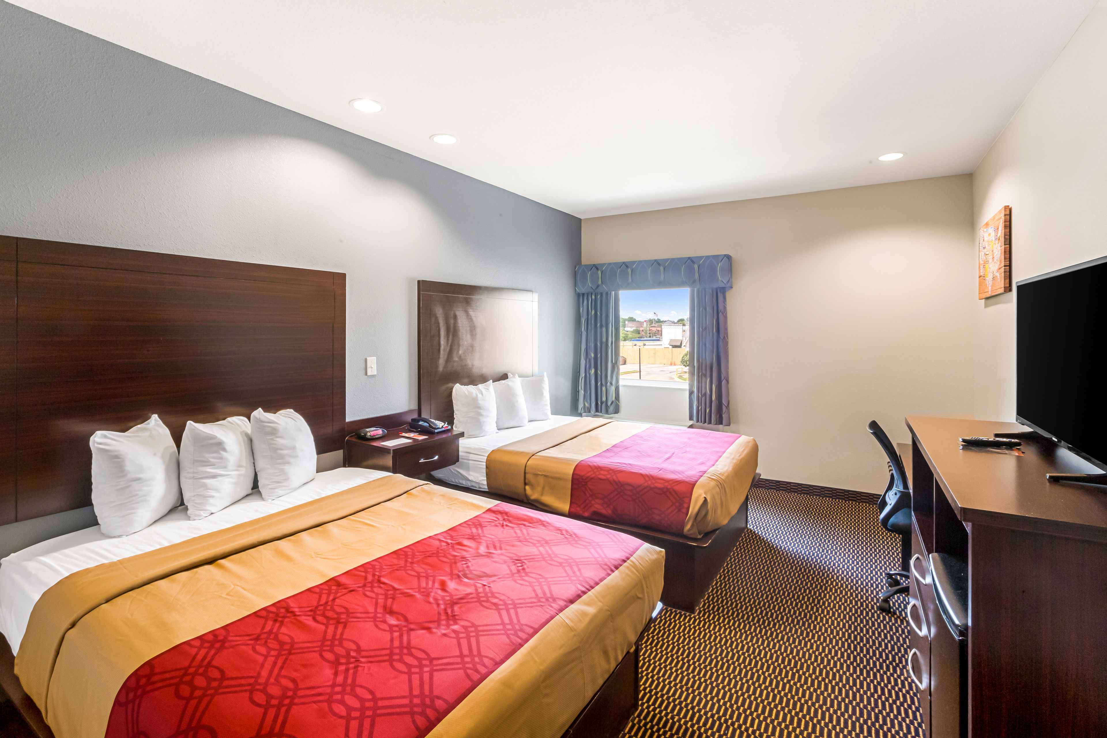A hotel room with two beds, a desk, a TV, and a window with curtains.