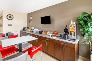 A modern kitchen with a white countertop, red and gray chairs, a coffee machine, and a television mounted on the wall.