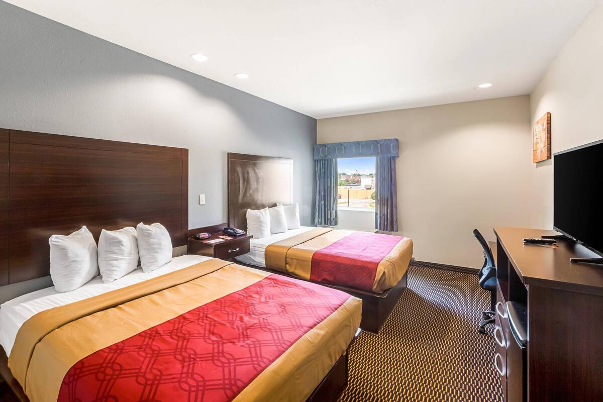 A hotel room with two beds, a desk, a television, and a window with curtains.