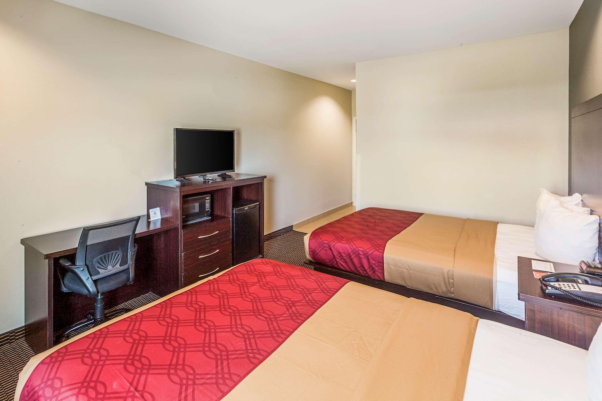 Habitación de hotel con dos camas, un escritorio con silla, televisor y teléfono.