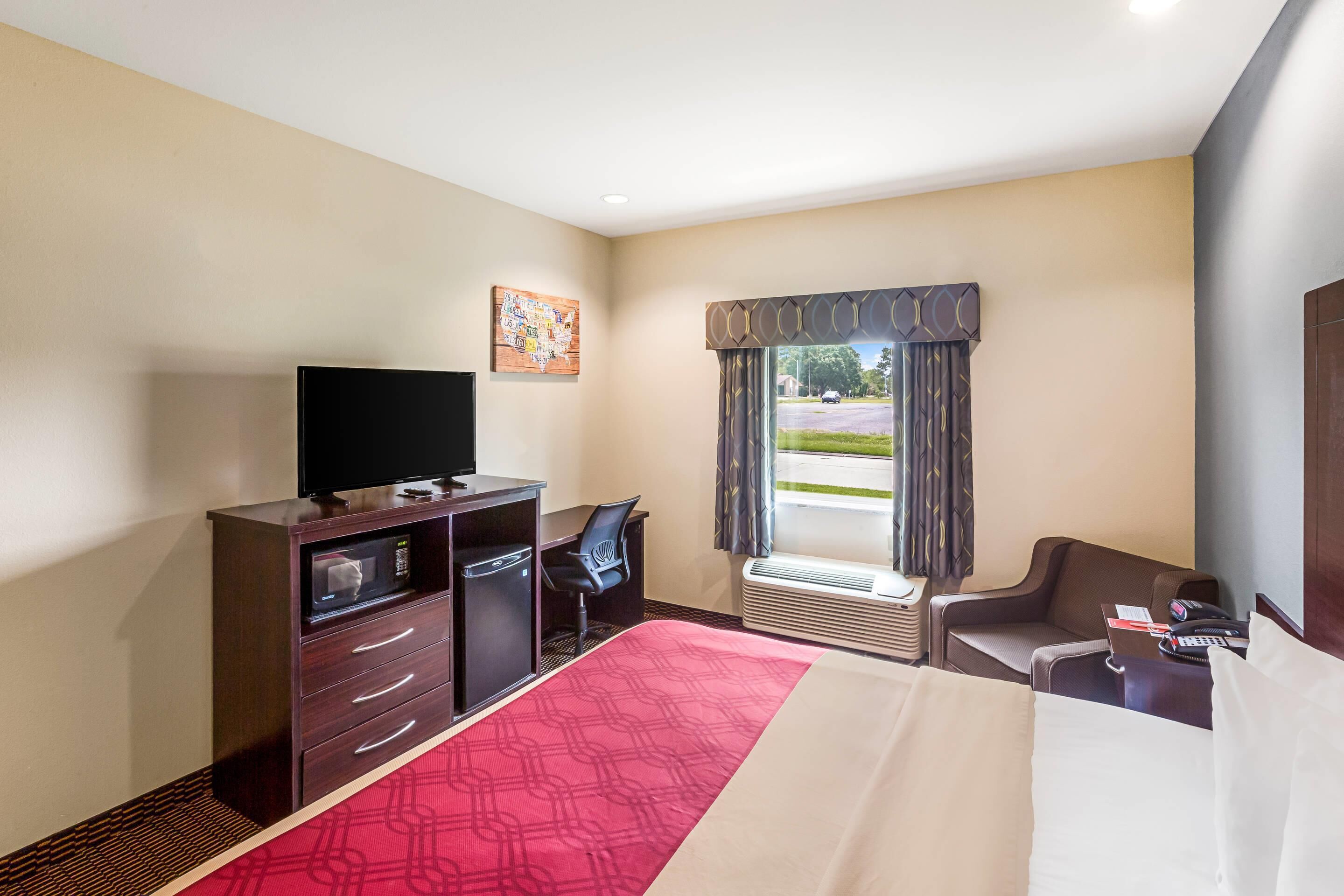 A hotel room with a bed, a desk with a computer, a TV, a chair, and a window with curtains.