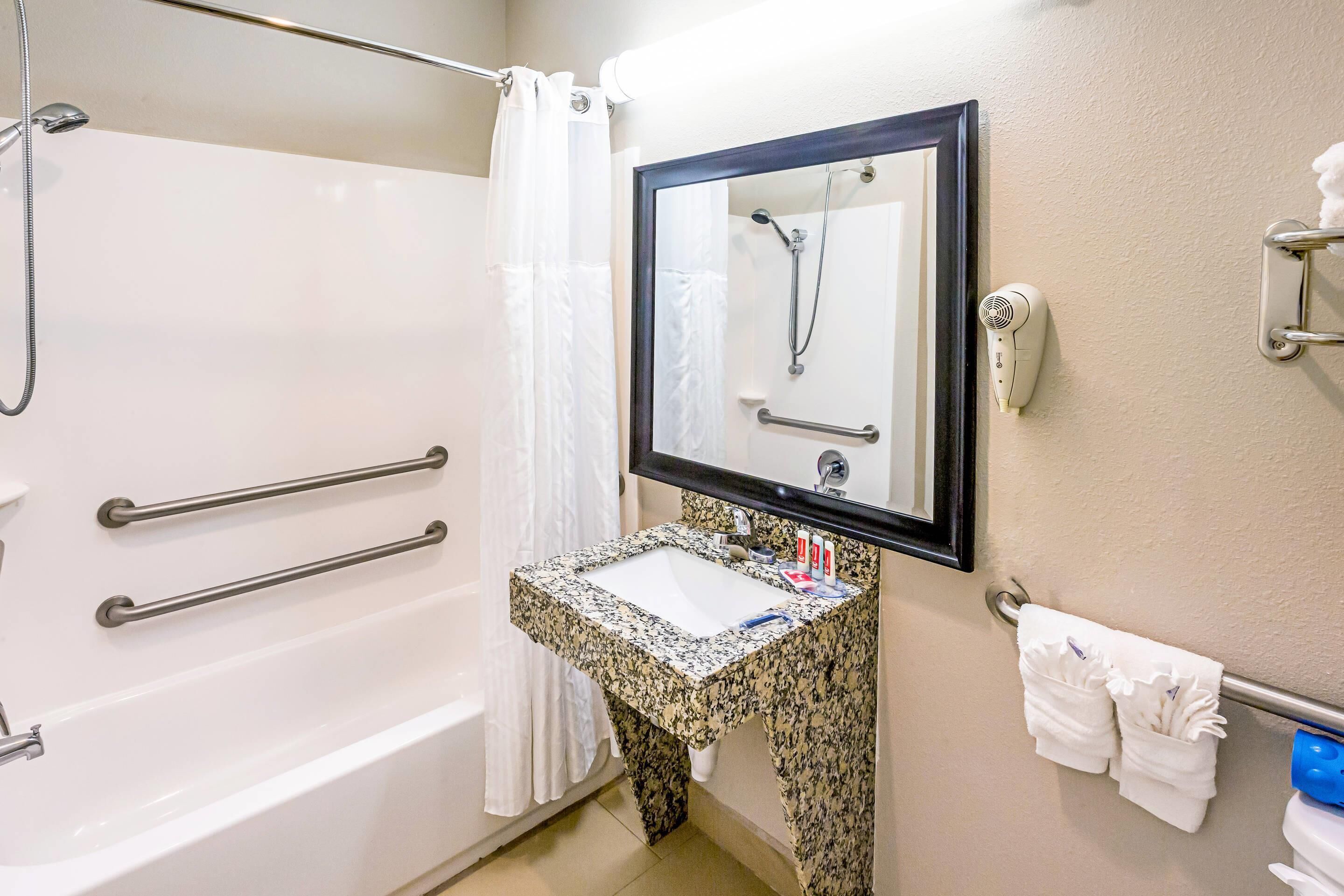 A bathroom with a white bathtub, a sink with a granite countertop, a mirror, and a towel rack.