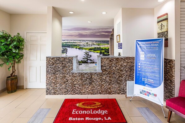 A reception area with a stone wall, a view of Baton Rouge, LA, a red carpet with the hotel name, and a promotional banner. - Econo Lodge Baton Rouge University Area (Baton Rouge)