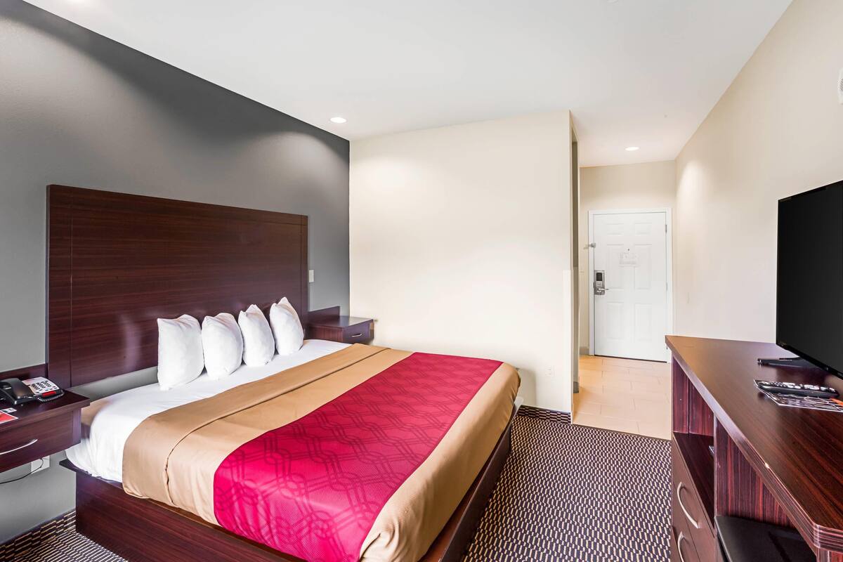 A hotel room with a large bed, a wooden headboard, a TV, and a desk with a telephone.