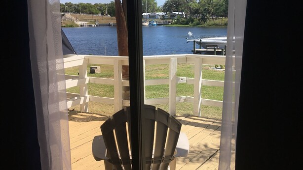 A deck with a chair, a view of a lake, and a white fence. - The Rivers Edge Motel (LaBelle)