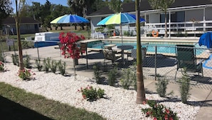 A pool area with a fenced pool, lounge chairs, and umbrellas. - The Rivers Edge Motel (LaBelle)
