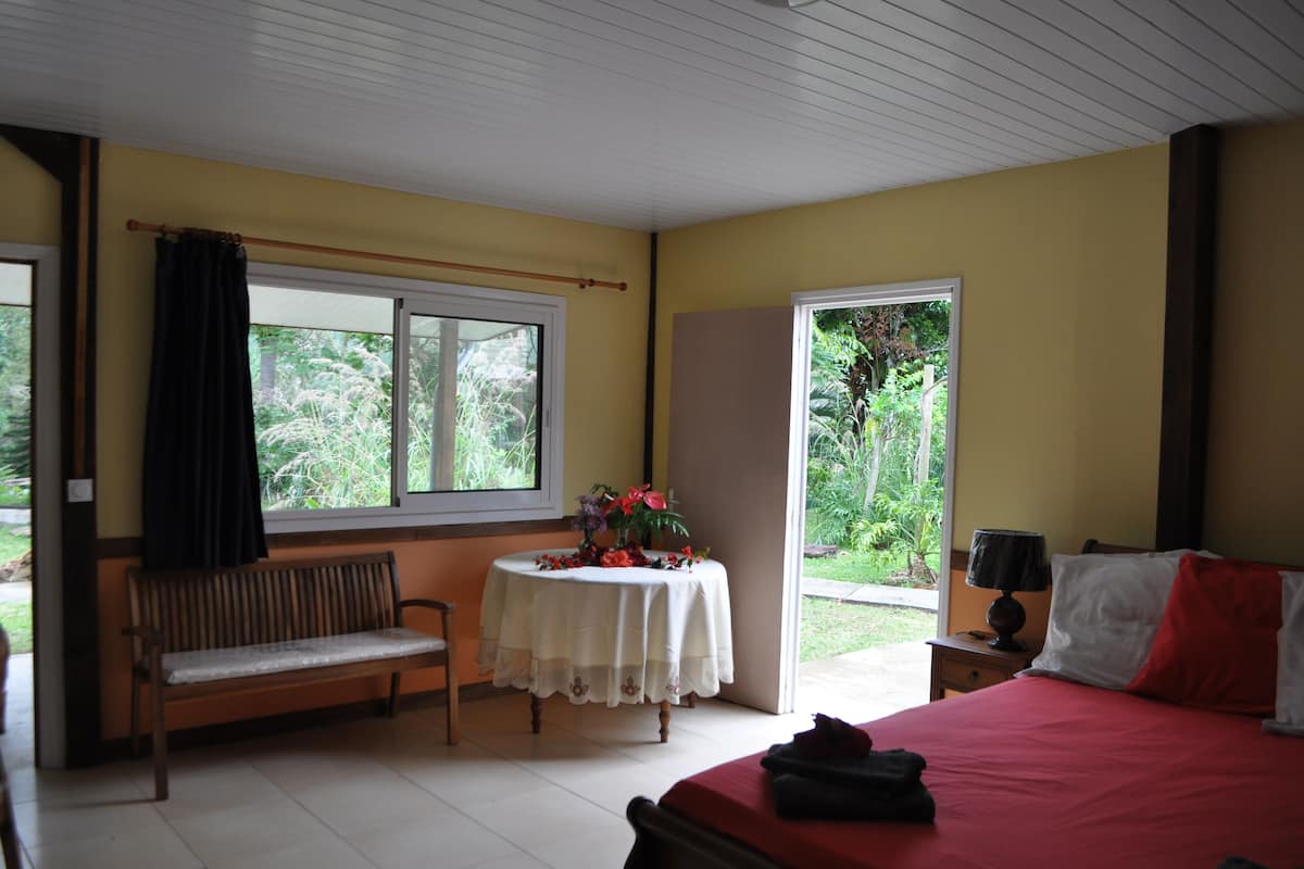 Un dormitorio con una cama, un banco, una mesa con flores y una ventana con cortinas.