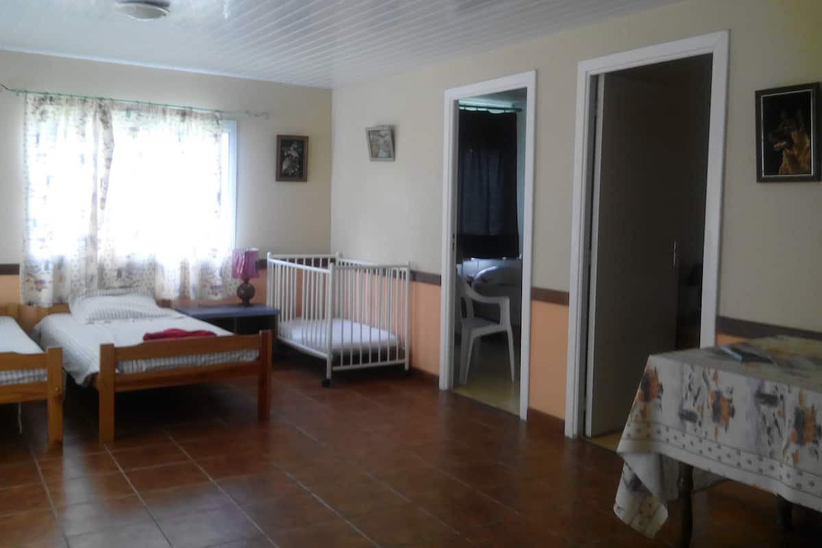 Una habitación con dos camas de madera, una cuna blanca, una mesa con mantel y una silla.
