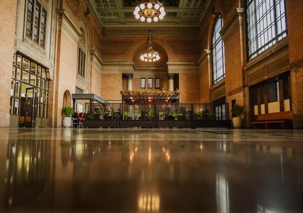 A spacious lobby with a polished floor, a central decorative area with plants, and a large chandelier. - Grand Central Hotel Auckland (Auckland)