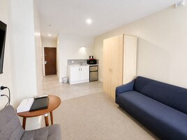 A modern living room with a sofa, a small table with a laptop, and a kitchenette in the background.