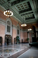 A spacious lobby with a high ceiling, ornate brick walls, and a patterned floor.