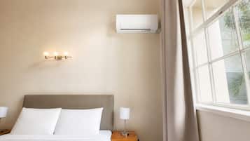 Habitación de hotel con cama, mesita de noche, lámpara, equipo de aire acondicionado y ventana con cortinas.