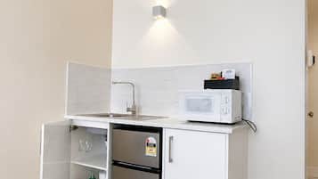 Une petite cuisine équipée d’un four à micro-ondes, d’un réfrigérateur et d’un petit placard contenant des verres à vin.