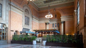 A spacious lobby with a high ceiling, brick walls, and a central seating area with plants.