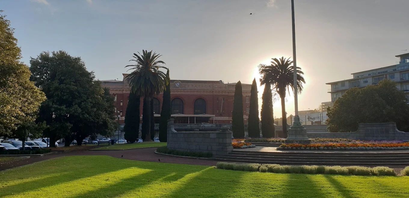 Un edificio con una torre de reloj, rodeado de un césped cuidado y palmeras.