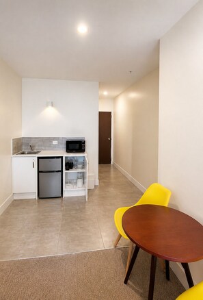A compact kitchen with a refrigerator, microwave, and a small sink. There is a dining area with a round table and two chairs. - Grand Central Serviced Apartments (Auckland)