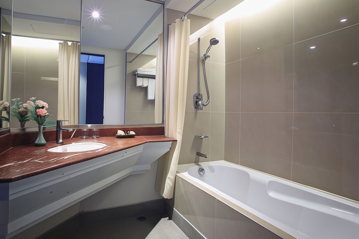 Un baño moderno con una bañera grande, un área de ducha separada y un tocador con lavabo y espejo.
