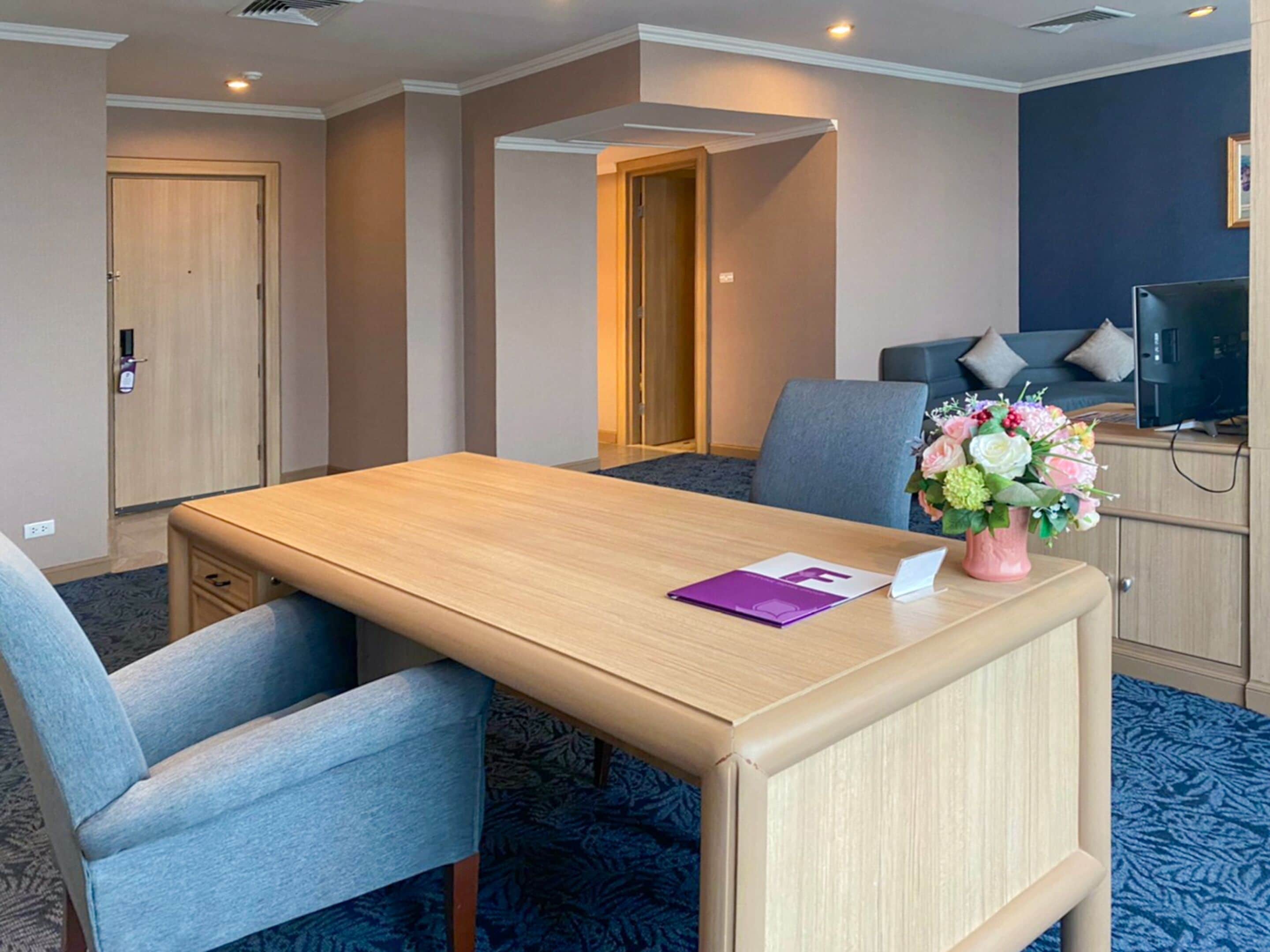 A hotel room with a wooden desk, two chairs, a television, and a floral arrangement.