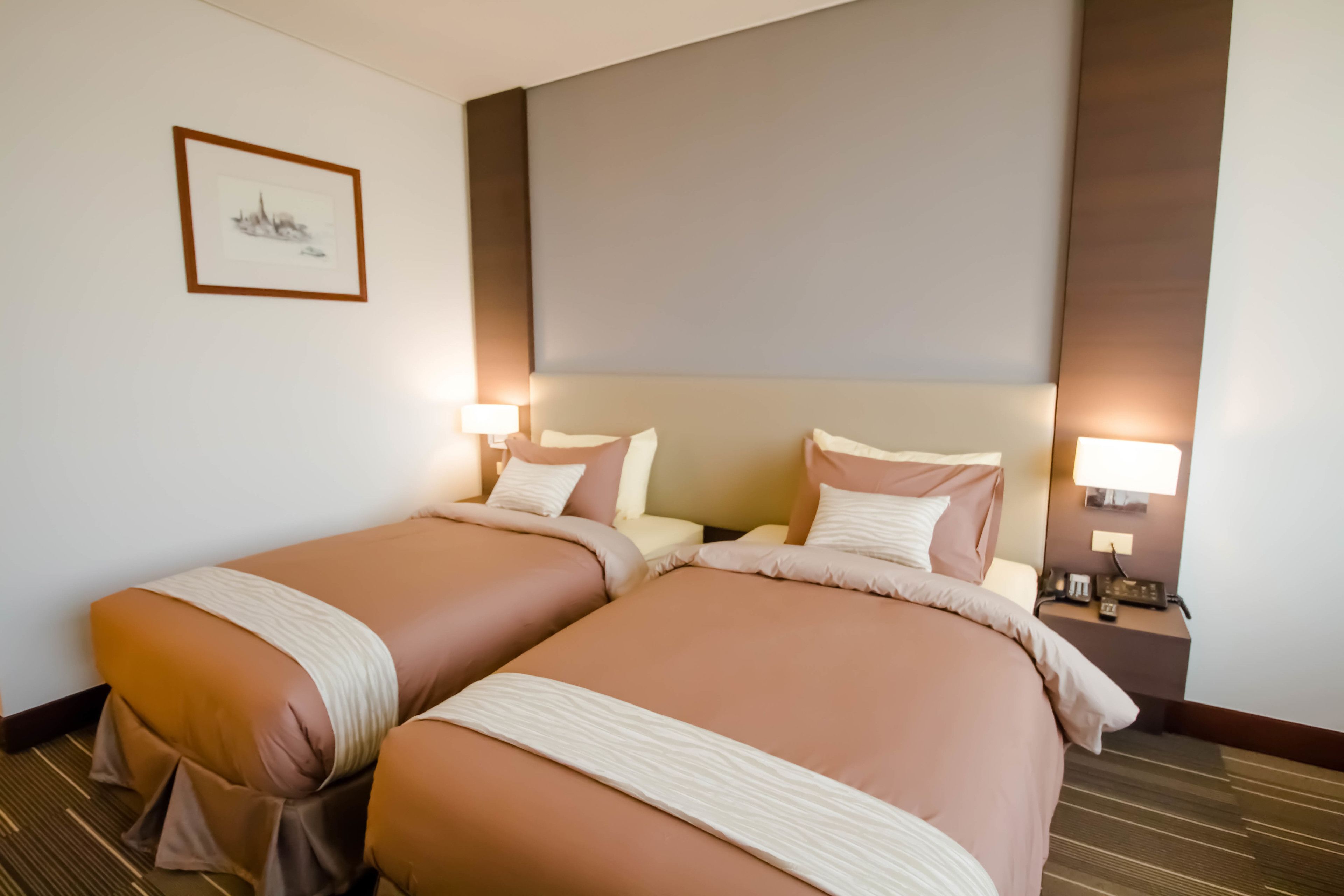 A hotel room with two beds, a framed picture on the wall, and bedside lamps.