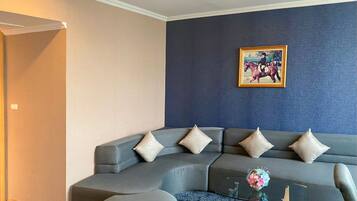 A modern living room with a grey sectional sofa, a round ottoman, and a glass coffee table.