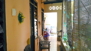A narrow corridor with benches and a small table, leading to a door with a gate. - Kost Semarang Peterongan Timur (Semarang)