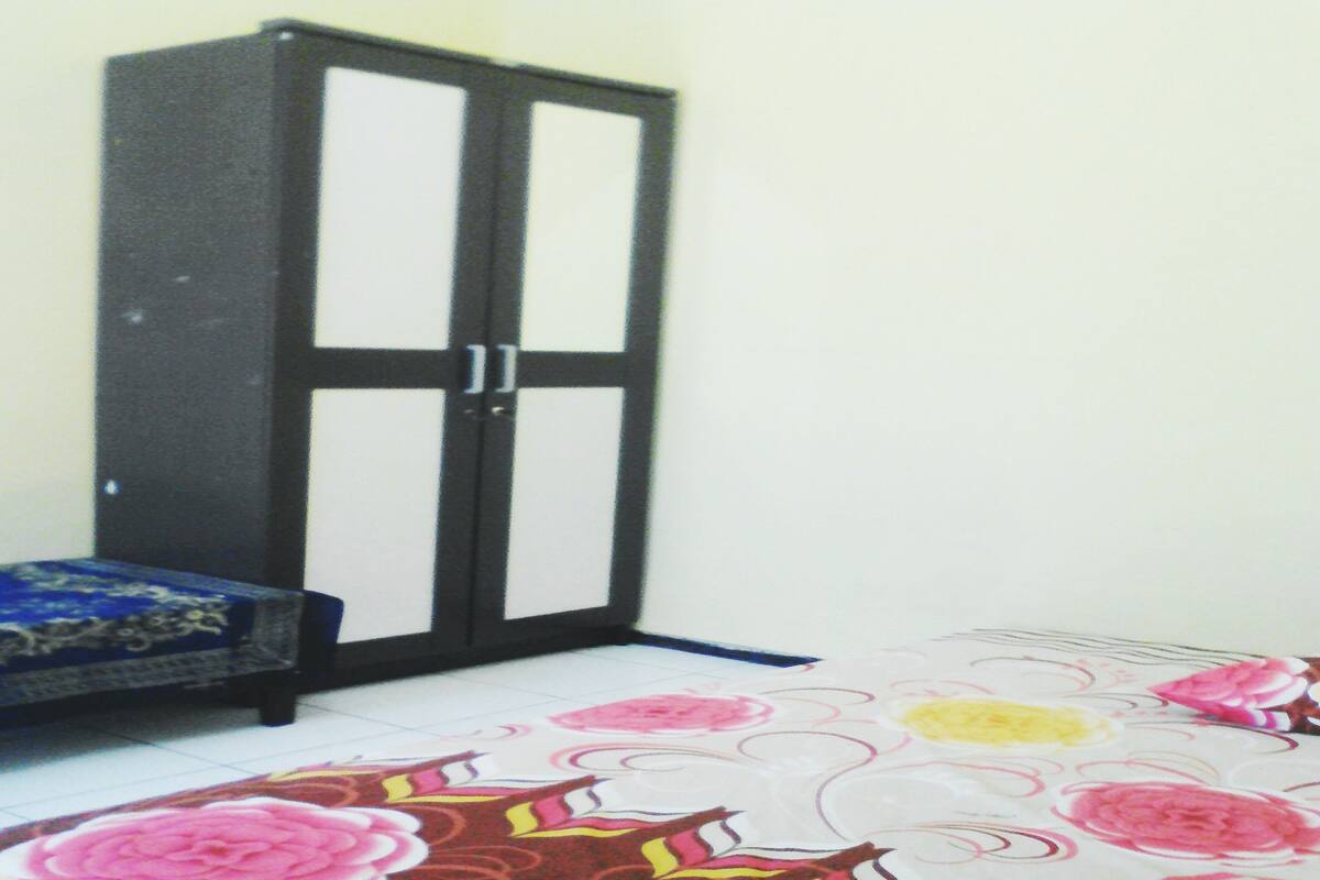 Quarto com guarda-roupa, cama com colcha florida e tapete estampado.