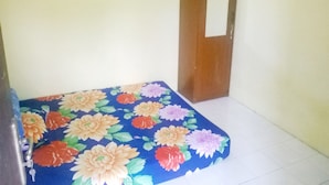 A room with a floral-patterned mattress on a white floor, a wooden door, and a plain wall. - Kost Semarang Peterongan Timur (Semarang)