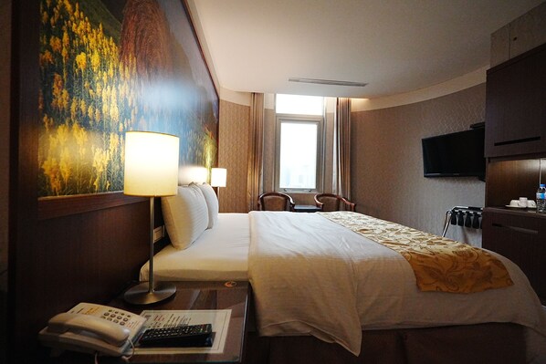 A hotel room with a bed, bedside lamps, a desk with a telephone and remote control, a television on the wall, and a window with curtains. - York Hotel (New Taipei City)