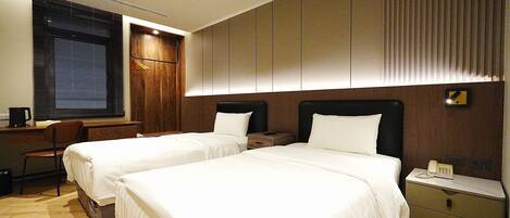 Habitación de hotel con dos camas, un escritorio, una silla y una mesita de noche con teléfono.