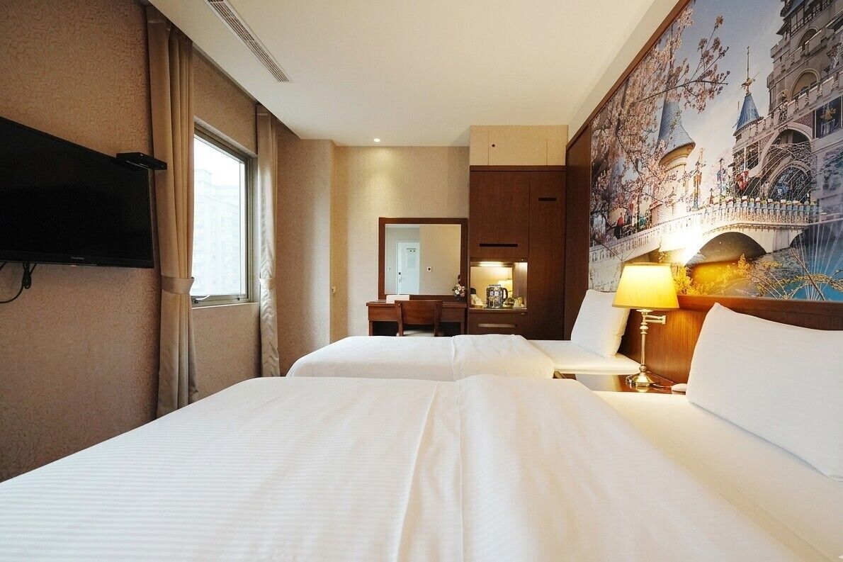 Hotelkamer met twee bedden, een televisie, een bureau, een stoel, een lamp en een groot muurschildering.
