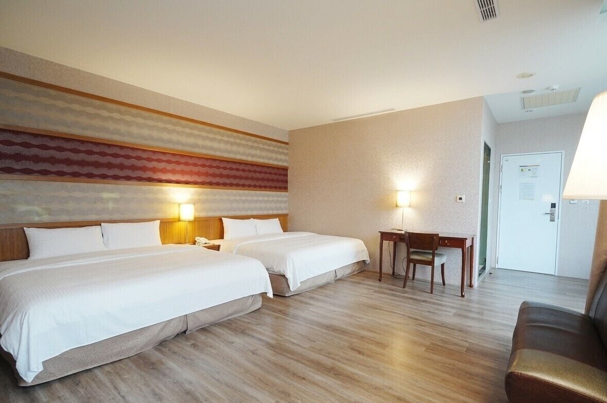 Une chambre d’hôtel avec deux lits, un bureau, une chaise et un canapé.