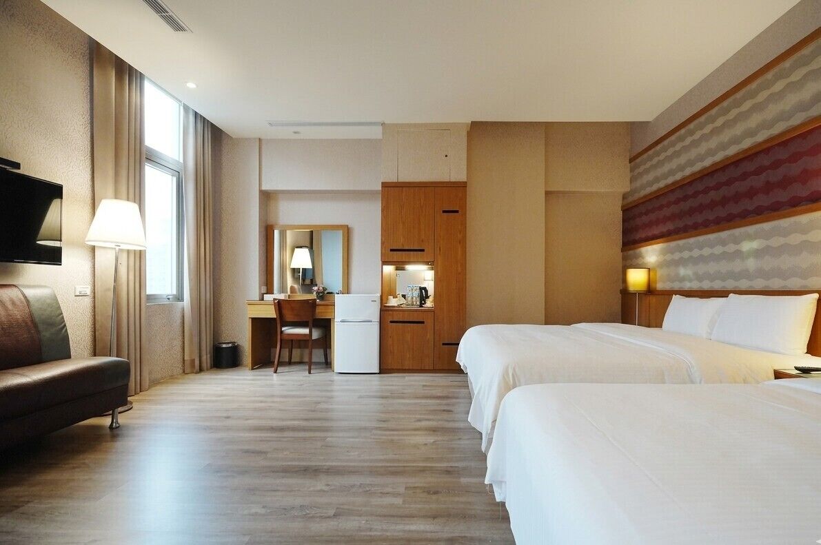Quarto de hotel com uma cama, uma escrivaninha, uma cadeira, uma televisão e uma janela.