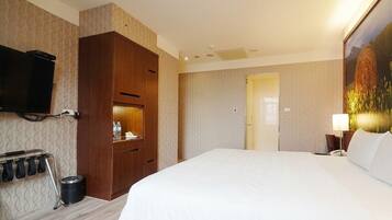 Quarto de hotel com uma cama grande, um guarda-roupa, uma televisão na parede, um quadro e uma porta que dá para outro cômodo.