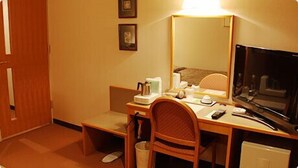 Een hotelkamer met een bureau, stoel, televisie en een kleine prullenbak.