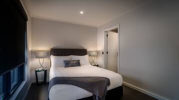 A modern hotel room with a large bed, two bedside tables with lamps, a window, and a door.