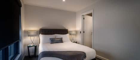 Una habitación de hotel moderna con una cama grande, dos mesitas de noche con lámparas, una ventana y una puerta.