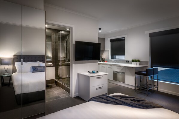 Una camera d'albergo moderna con un letto grande, un armadio a muro, un bagno con doccia in vetro, una scrivania con un computer e un'ampia finestra.