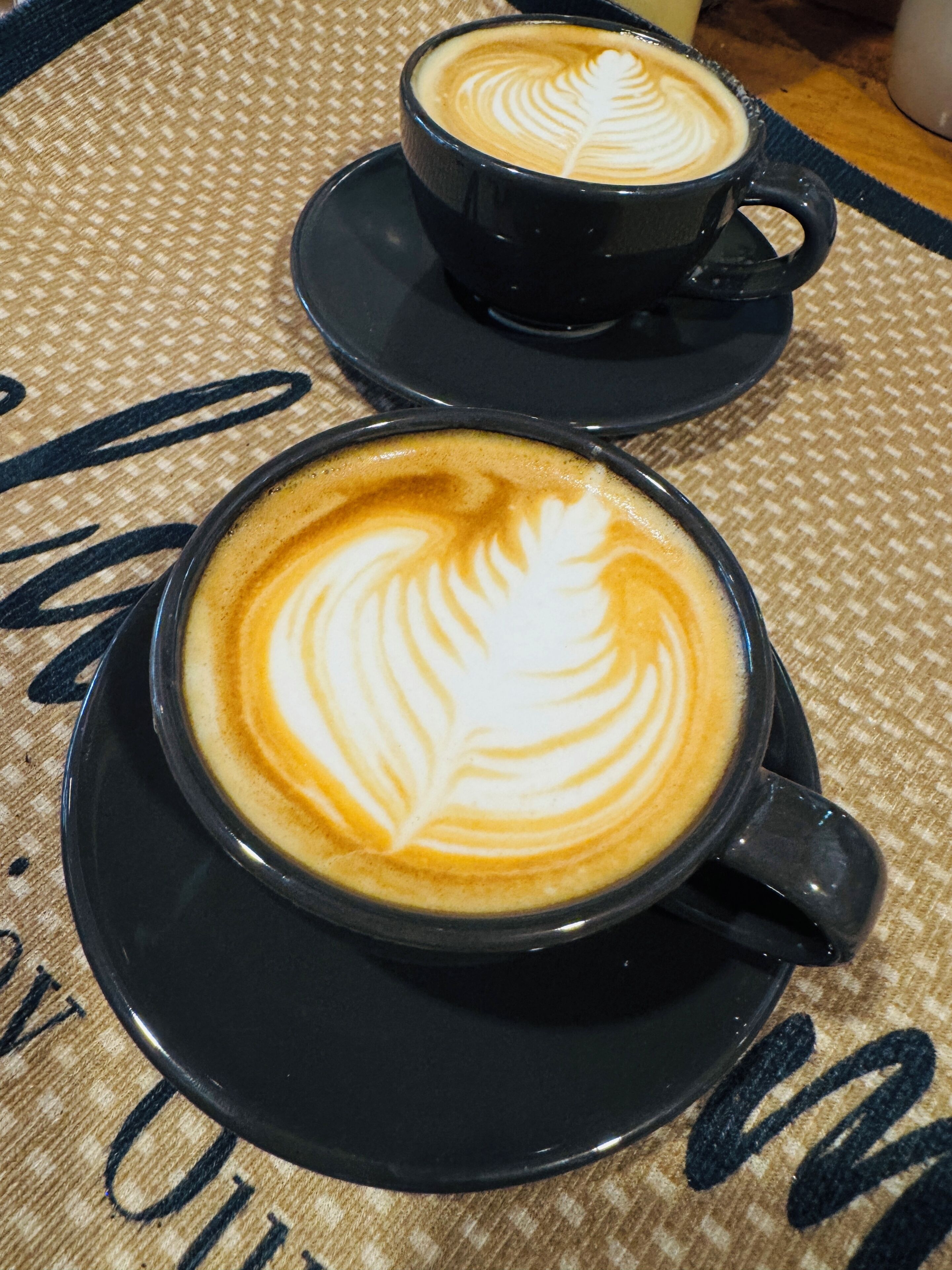 Duas xícaras de café preto com arte de latte sobre uma toalha de mesa trançada.