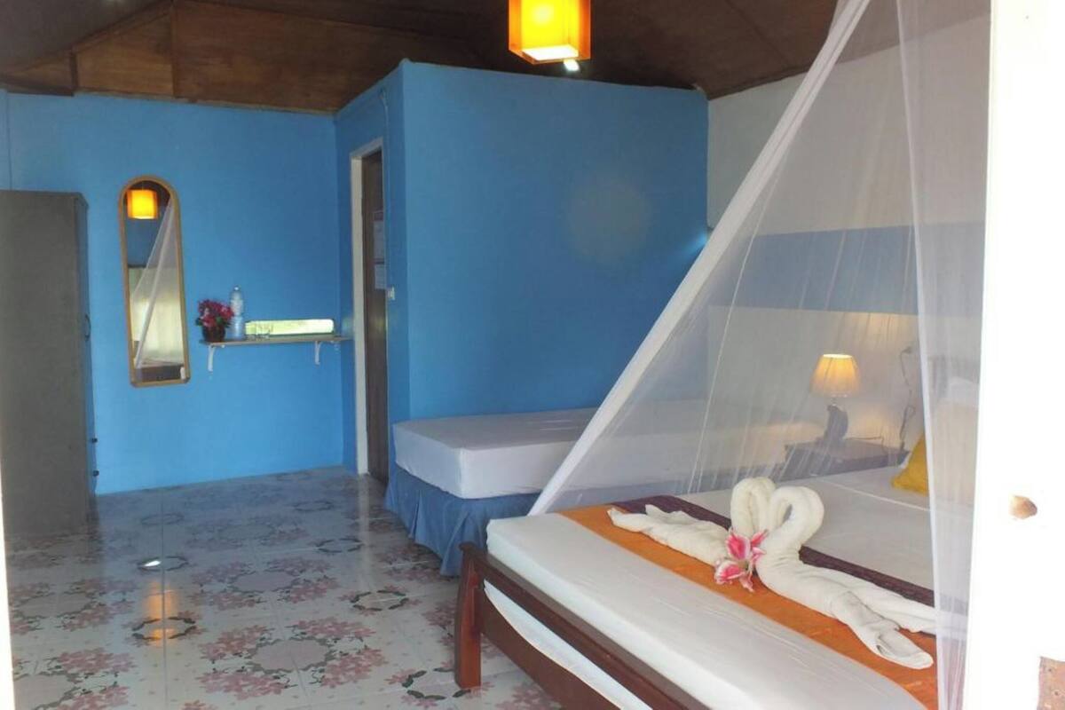 Een slaapkamer met een bed, nachtkastje, spiegel en raam met klamboe.