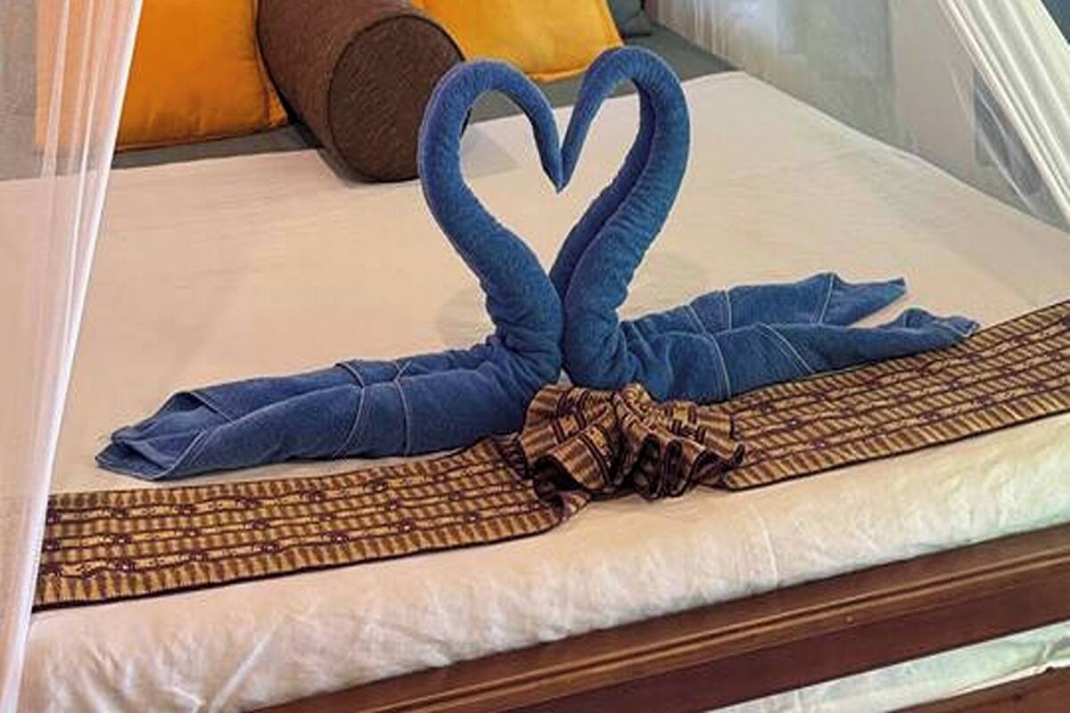 Een bed met klamboe, blauwe handdoeken en een handdoekopstelling in hartvorm.