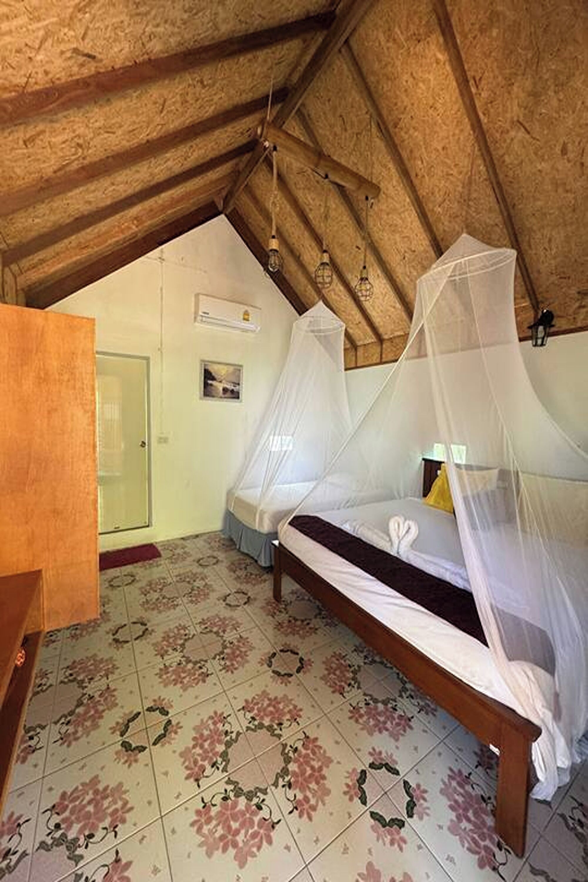 Een slaapkamer met een houten plafond, een bed met klamboe en vloertegels met een bloemenprint.